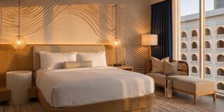 A stylish bedroom bathed in warm sunset light, featuring a cozy bed, modern furnishings, and large windows with a view.