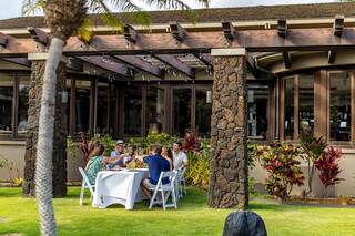 A group of friends enjoys a meal outdoors at a scenic venue, surrounded by lush greenery and a charming stone structure.