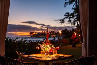 A romantic dinner setting on the beach, featuring a beautifully lit table with tropical flowers, against a stunning sunset backdrop.