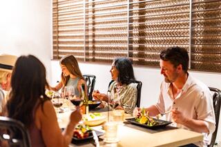A group enjoys a lively dinner, sharing dishes and laughter, with glasses of wine and a warm, inviting atmosphere.