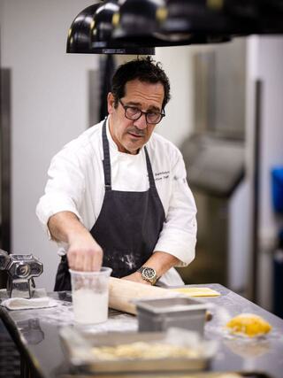 A chef in an apron diligently prepares food in a professional kitchen, using flour and equipment on the counter.