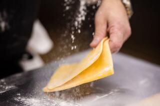 A hand dusts flour over a freshly prepared sheet of pasta, showcasing the delicate process of making homemade dough.