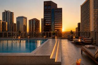 A tranquil rooftop pool at sunset, surrounded by modern skyscrapers, creating a serene atmosphere with drinks and cozy seating.