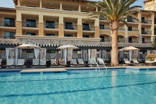 A serene poolside scene features cozy lounge chairs and cabanas beside a shimmering pool, with a hotel and palm trees in the background.