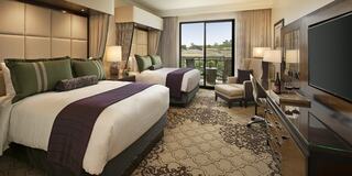 A cozy luxury hotel room features a large bed with plush pillows, a desk, lamps, and a balcony overlooking the scenery. Elegant decor enhances the ambiance.