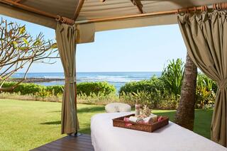A tranquil spa setting features a massage table with fresh towels, surrounded by lush greenery and a serene ocean view.