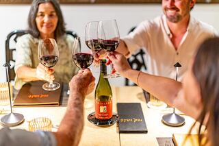 An elegant outdoor dining setup features long wooden tables adorned with white linens and twinkling lights, set against a scenic backdrop.