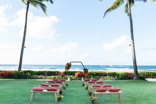 A serene outdoor venue featuring rows of white chairs, a decorative gazebo, and a backdrop of lush vineyards under a clear blue sky.