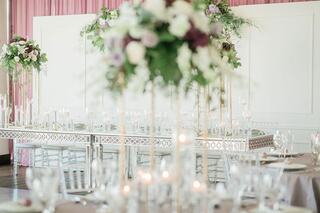 Elegant tables adorned with floral arrangements and candles create a romantic atmosphere, complemented by soft pink drapery in the background.