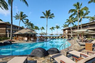 A serene poolside scene with palm trees, lounge chairs, and a vibrant sky, inviting relaxation in a tropical resort setting.