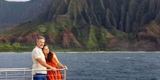 A couple embraces on a boat, gazing at lush green mountains and calm waters, creating a romantic and scenic atmosphere.