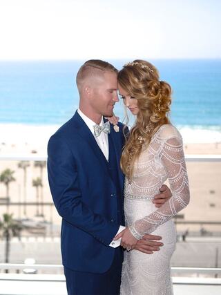 A happy couple shares an intimate moment, with a beach backdrop and elegant attire, radiating love and joy on their special day.