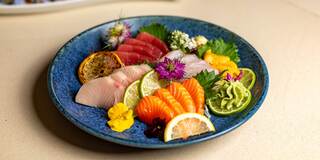 A vibrant assortment of sashimi, featuring colorful slices of fish, garnished with lime, edible flowers, and decorative herbs.
