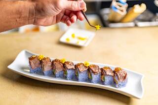 A gourmet dish features a juicy steak topped with lobster, asparagus, and a creamy sauce, accompanied by elegant sides and a cocktail.