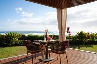 A cozy table for two with tropical flowers overlooks a stunning ocean view, framed by lush greenery under a clear blue sky.