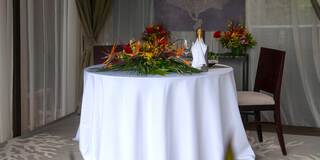 An elegantly set round table adorned with tropical flowers, a bottle, and a chair, creating a serene dining atmosphere.