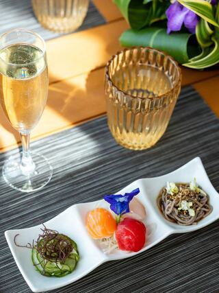 A stylish platter features colorful sushi, garnished with vibrant flowers, alongside a glass of sparkling drink and an elegant amber-toned glass.