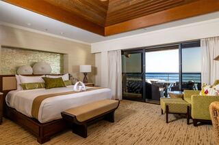 A stylish bedroom with a spacious bed, decorative accents, and a balcony offering ocean views. Plush seating enhances the cozy atmosphere.