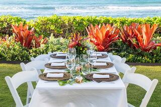 A beautifully set dining table with elegant glassware and vibrant floral centerpieces, overlooking lush greenery and the tranquil sea.