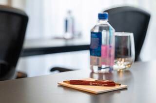 A polished table features a pen resting on a notepad, with a water bottle and glass nearby, creating a professional environment.