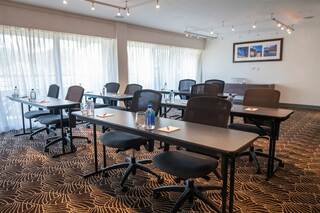 A modern, well-lit conference room with rows of tables and chairs, featuring water bottles and notepads on each table.