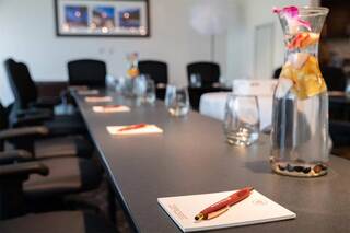 A conference room setup featuring a long table, chairs, water carafe with fruit, glasses, and notepads with pens.