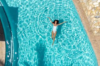 A person floats peacefully in a crystal-clear pool, enjoying the sun and vibrant reflections on the water's surface.