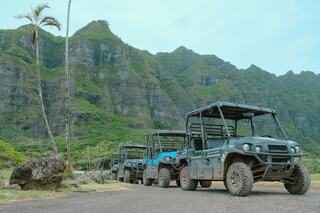 Off-road vehicles lined up against a backdrop of lush green mountains and a clear sky, showcasing nature's beauty and adventure opportunities.