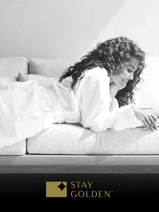 A woman in a white robe relaxes on a couch, smiling as she enjoys her time reading