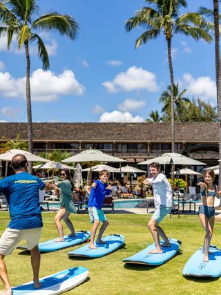 A group of people practicing stand-up paddleboarding on blue boards, surrounded by palm trees and a sunny resort atmosphere.