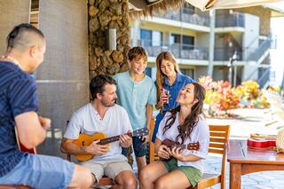 A cheerful group plays ukuleles together outdoors, sharing smiles and laughter, creating a fun and relaxing atmosphere.