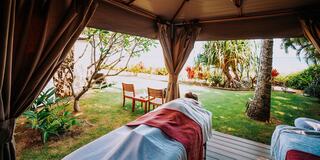 A serene outdoor spa setting features a massage bed surrounded by lush greenery and tropical plants, enhancing relaxation and tranquility.