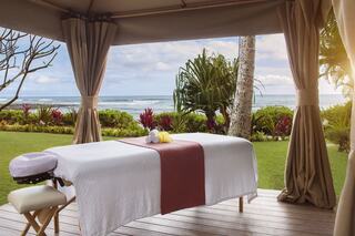 A tranquil outdoor spa setup features a massage table overlooking lush greenery and the ocean, creating a serene and relaxing atmosphere.