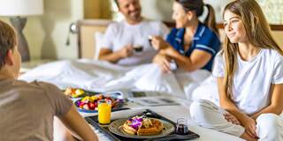 A family enjoys a cozy breakfast in bed, featuring waffles and fruit, while sharing smiles and conversation.