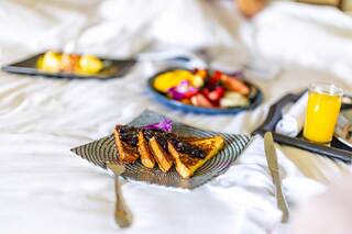 A cozy breakfast spread features French toast with fruit, a colorful plate of berries, and a glass of juice, all on a bed.
