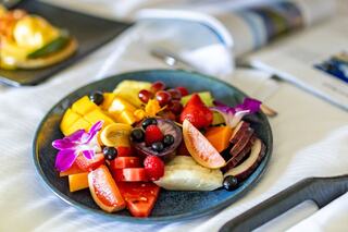 A vibrant fruit platter featuring a variety of colorful fruits, garnished with edible flowers, arranged beautifully on a blue plate.