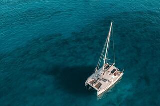 A sailboat glides peacefully over crystal-clear turquoise waters, casting a gentle shadow beneath its hull.