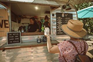A woman in a straw hat orders a treat at a food truck, while friendly staff serve in a sunny outdoor setting.