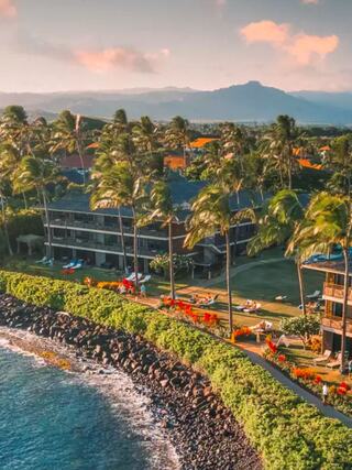 A tropical resort with lush palm trees, vibrant landscaping, and ocean views, set against a backdrop of distant mountains and a serene coastline.