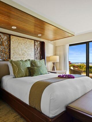 A stylish bedroom features a cozy bed with decorative pillows, elegant wood accents, and a stunning view through large windows.