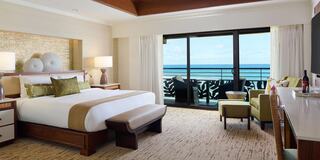 A stylish hotel room featuring a king-sized bed, cozy seating area, and large windows with an ocean view. Elegant and inviting decor.