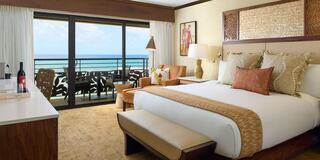 A stylish hotel room features a king-sized bed, elegant decor, a cozy seating area, and a stunning ocean view from the balcony.