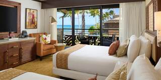 A stylish hotel room features two beds, modern decor, and a balcony with stunning ocean views framed by palm trees. Comfort meets elegance.