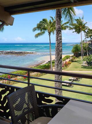 A beautiful coastal view features palm trees swaying over clear blue waters, with lush greenery and lounge chairs along the beach.