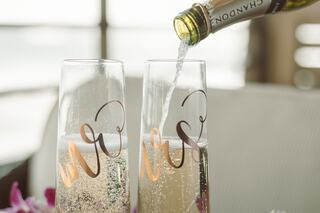 Two elegant flutes labeled "Mrs." are filled with sparkling champagne, capturing a celebratory moment. Bubbles rise as champagne is poured.