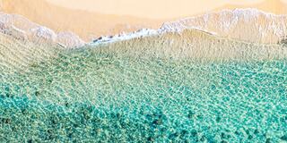 Gentle waves meet a sandy shore, revealing a gradient of clear turquoise water that transitions to deeper blue hues.