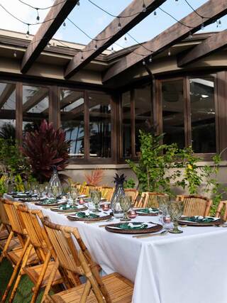 A beautifully set outdoor dining table with bamboo chairs, elegant dishware, greenery, and string lights overhead, creating a welcoming atmosphere.