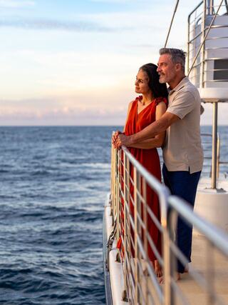 A couple gazes at the ocean, enjoying a serene moment together on a yacht during sunset, exuding romance and tranquility.