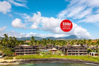 A tropical resort features lush palm trees, an inviting pool area, and stunning ocean views under a bright blue sky with fluffy clouds.