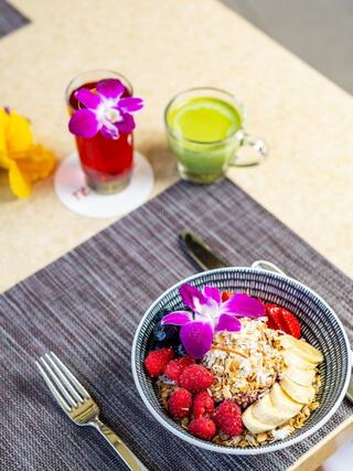 A vibrant bowl of granola topped with fruits and flowers, accompanied by colorful drinks, set on a stylish table.